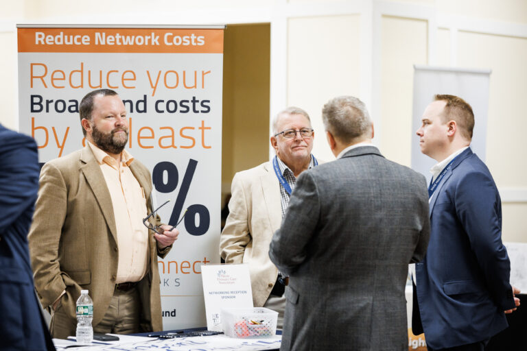 HealthConnect Networks team members standing at an exhibit booth promoting Healthcare Connect Fund funding opportunities at a healthcare conference.